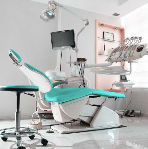 Blue and white dentist chair with screen and medical instruments sitting in white doctors office.