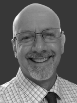 black and white photo of middle aged man with glasses, no hair, grey facial hair and striped patterned shirt with dark tie